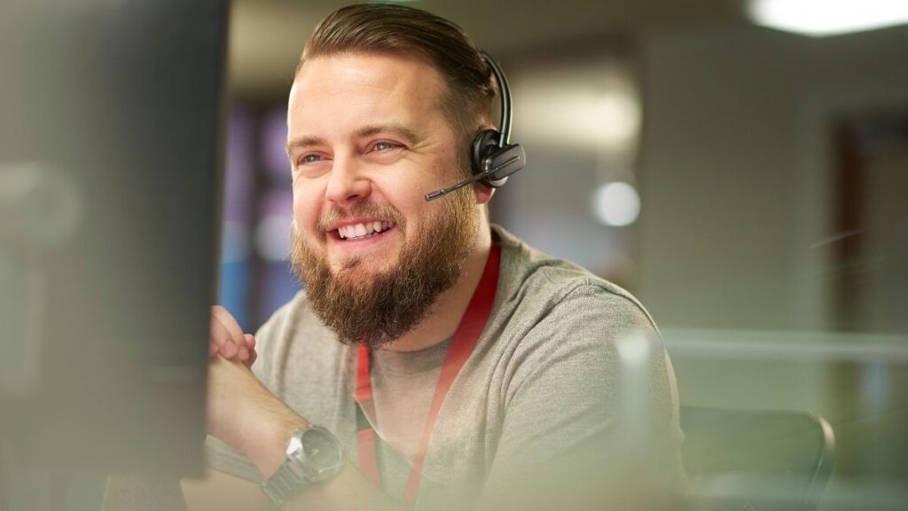 male IT support employee with beard wearing phone headset and smiling