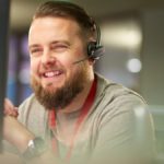 male IT support employee with beard wearing phone headset and smiling