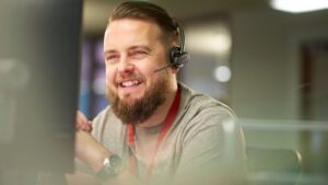 male IT support employee with beard wearing phone headset and smiling