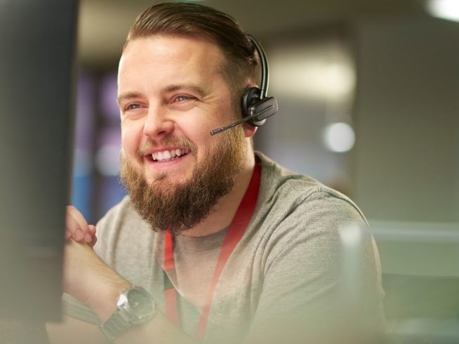 male IT support employee with beard wearing phone headset and smiling