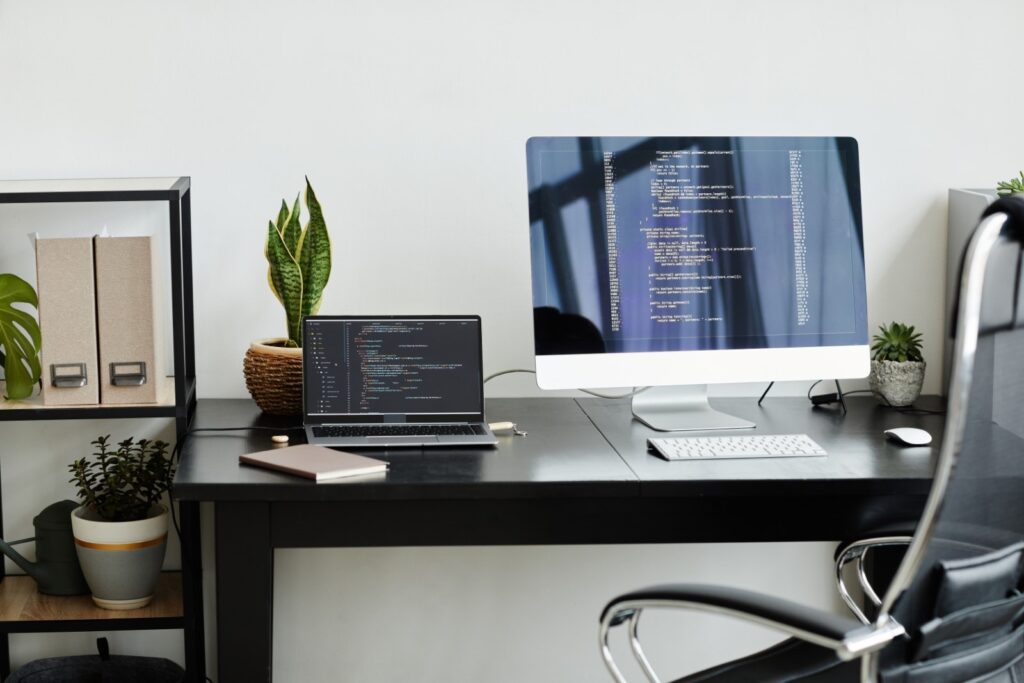 an office desk with a laptop and desktop computer both displaying code