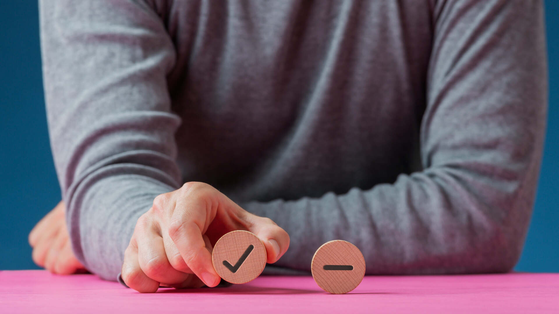 A man picking up a wooden circle with a tick symbol on it, next to it is a wooden circle with a minus symbol