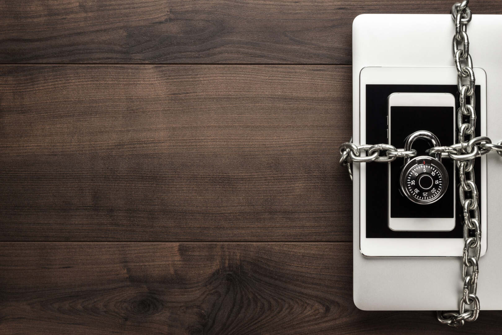 a laptop, phone, and tablet locked by a padlock and chain representing cybersecurity